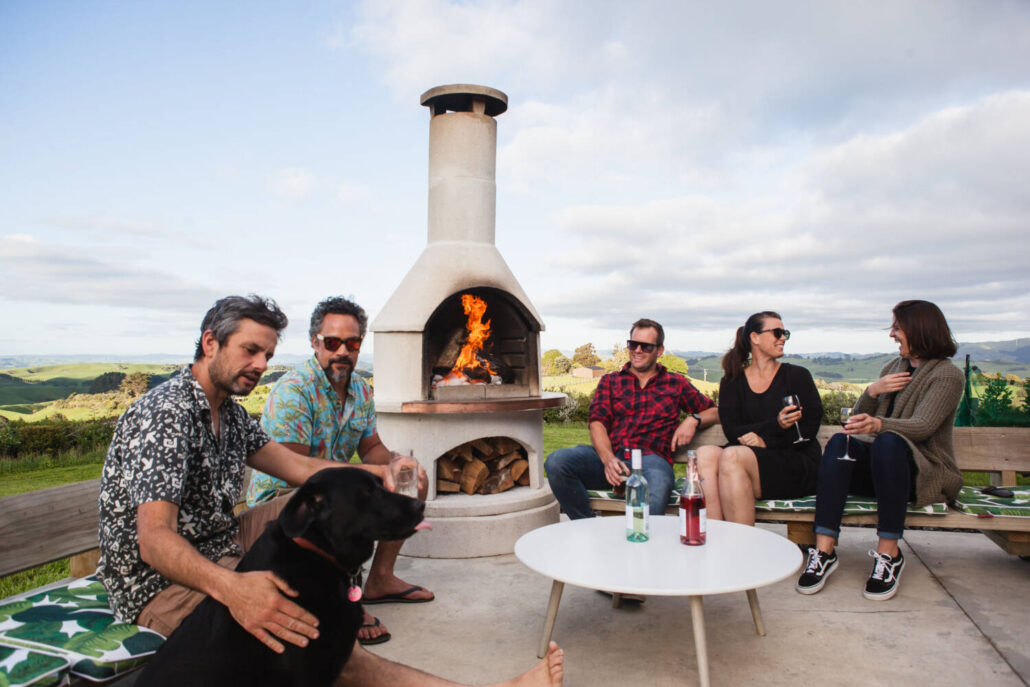 Friends sharing drinks around the Buschbeck outdoor fireplace.